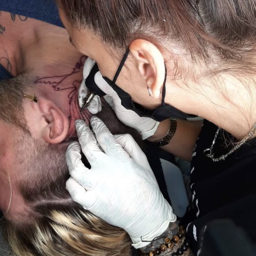 Tätowiererin bei Magic Pain Wiesloch tätowiert präzise Linien auf den Hals eines Kunden unter Beachtung von Hygienestandards.